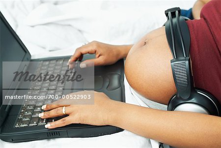 Pregnant Woman Using Laptop, Using Headphones on Belly - Stock