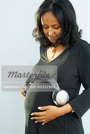 Pregnant woman holding headphones at her belly stock photo