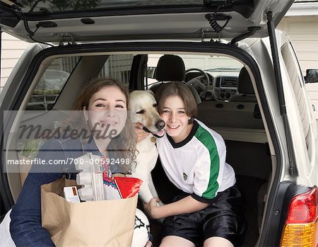 Mother and Son Sitting in Back of Minivan with Dog and Groceries.
