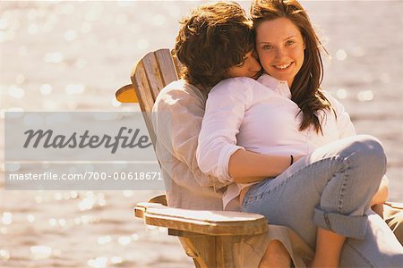 Young Couple Cuddling In An Adirondack Chair On The Beach