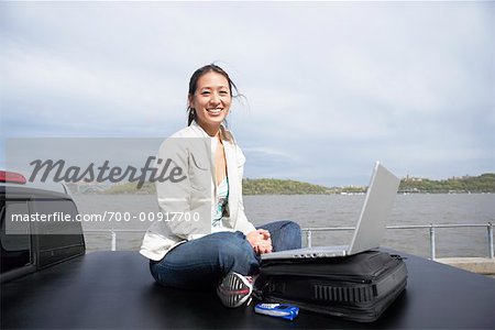 Woman Sitting on Back of Truck Using Laptop