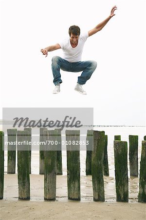 Man Jumping on Wooden Posts on Beach