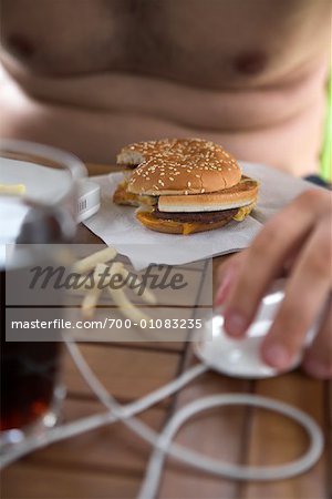 Man Using Computer and Eating Hamburger with Fries