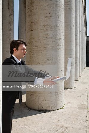 Businessman Holding Laptop Computer by Pillars