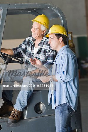 Construction Worker With Clipboard Talking to Worker on Forklift