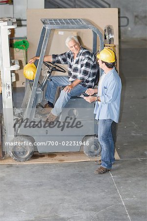 Construction Worker With Clipboard Talking to Worker on Forklift