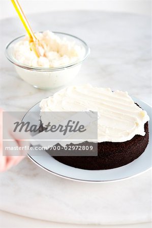 Person Icing a Chocolate Cake