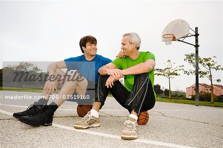 Father and Son Sitting on Basketballs on Court