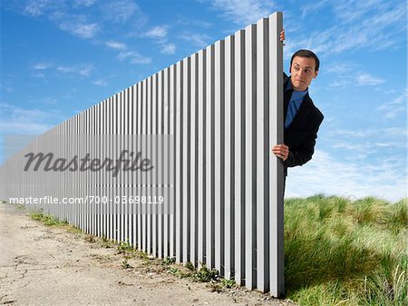 Businessman Peeking Out from Behind Eternal Fence