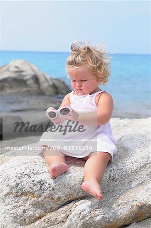 Little Girl with Sunglasses Sitting on Rock