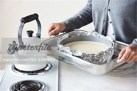 Woman Holding Pan with Cheesecake Batter next to Kettle