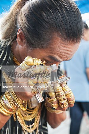 Man Wearing Lots of Jewelry Looking at Amulet Through Loupe