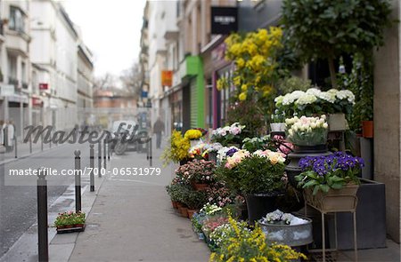 Selective focus on colourful spring flower stall on Paris sidewalk with pedestrians walking and other shops in background