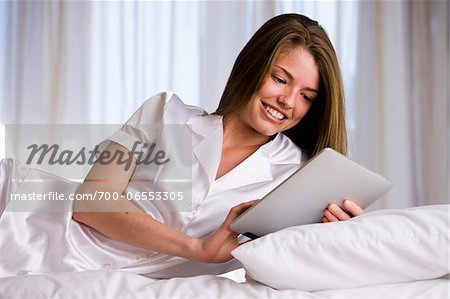 Woman lying on bed in her bedroom using digital tablet computer
