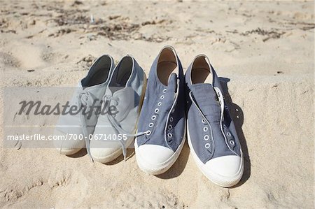 Two pairs of blue sneaker shoes on sand at the beach