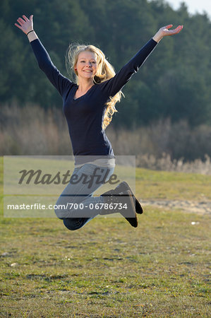 Happy blond Teenage Girl jumping in the air outdoors in an autumn landscape, Bavaria, Germany