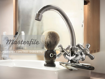 Straight razor and shaving brush on edge of bathroom sink with blood type indicated on shaving brush