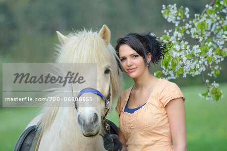 Portrait of a young woman with a icelandic horse standing under a flowering cherry tree in spring, Germany