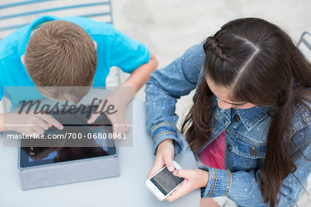 High Angle View of Boy with iPad and Girl with iPhone outside.