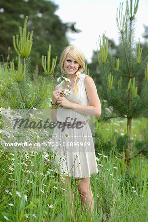 Portrait of blond woman holding oxeye daisy flowers in meadow, Germany