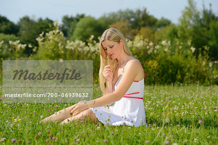 Young woman sitting in a meadow in summer, Bavaria, Germany.