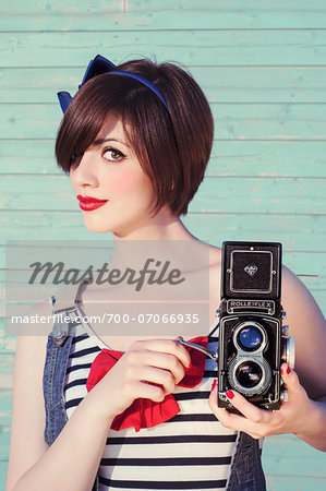 Portrait of young woman looking at camera and holding vintage camera, studio shot