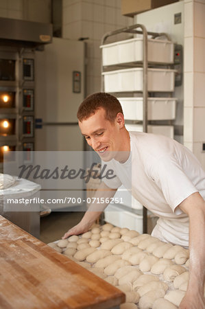 Male baker lifting tray of bread dough lumps in bakery, Le Boulanger des Invalides, Paris, France