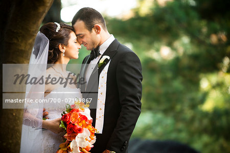 Portrait of bride and groom standing outdoors next to trees in public garden, face to face and smiling, in Autumn, Ontario, Canada