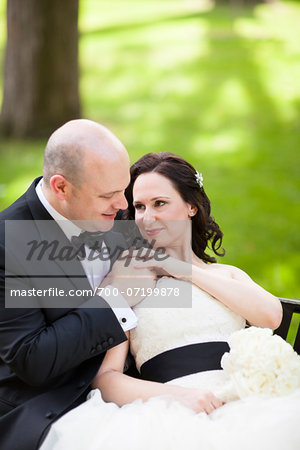 Portrait of bride and groom sitting outdoors in garden, holding hand, smiling and looking at each other, Ontario, Canada