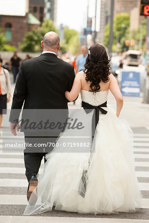 Backview of bride and groom walking across intersection of city street, Toronto, Ontario, Canada