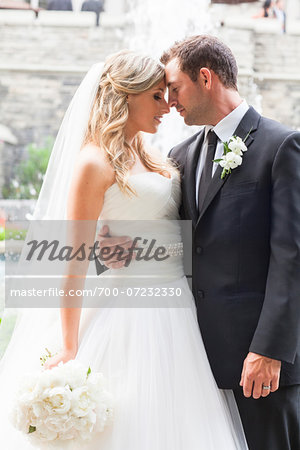 Portrait of Bride and Groom standing face-to-face outdoors with arms around each other on Wedding Day, Canada
