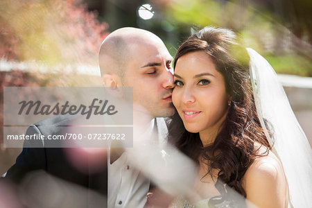 Close-up portrait of groom gving bride a kiss on cheek, sitting outdoors on Wedding Day, Canada