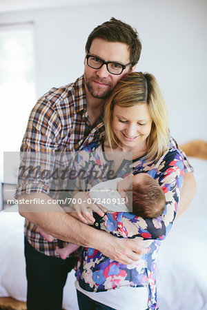 Portrait of Mom and Dad holding newborn, baby boy standing in bedroom, USA