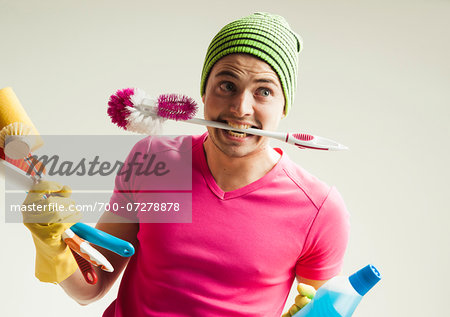 Close-up portrait of young man goofing around and holding colorful cleaning supplies, studio shot on white background
