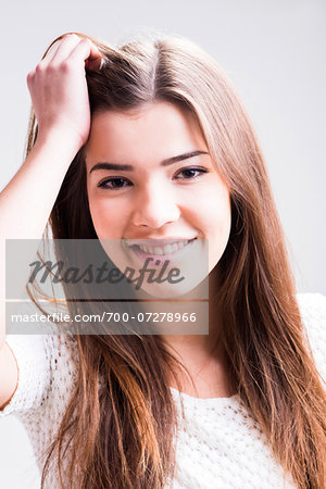 Close-up portrait of young woman with long, brown hair, smiling and looking at camera, studio shot on white background