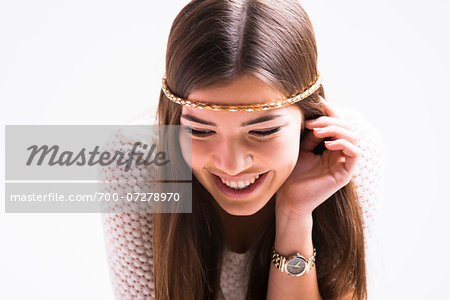 Portrait of young woman with long, brown hair, wearing headband, smiling and looking downwards, studio shot on white background