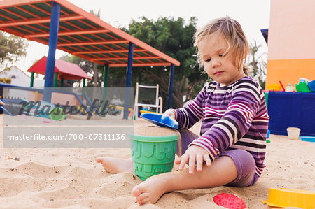 Three year old girl playing in playground with a shovel and bucket in sand, Spain