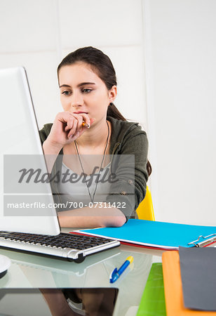 Teenager girl sitting at desk looking at desktop computer monitor, studio shot