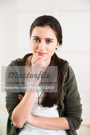 Portrait of teenage girl with arms crossed and hand on chin, looking at camera and smiling, studio shot on white background