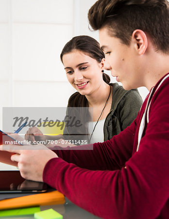 Teenage boy and teenage girl working on project using tablet computer and file folders, studio shot