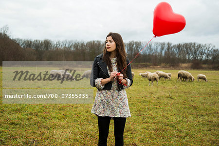 Young Woman with Heart-shaped Balloon by Sheep in Field, Mannheim, Baden-Wurttemberg, Germany
