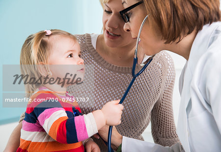 Doctor using Stethoscope on Baby Girl with Mother in Doctor's Office