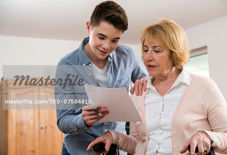 Teenage boy helping Grandmother sitting in walker at home, filling out paperwork, Germany