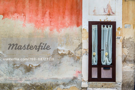 Worn, stone walls of a building with curtained door in Ragusa in Sicily, Italy