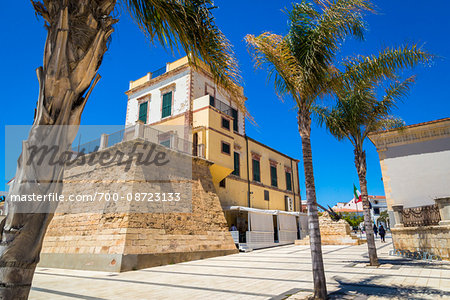 Stone buildings of Torre Cabrera and walkway with palm trees in Marina di Ragusa in Sicily, Italy