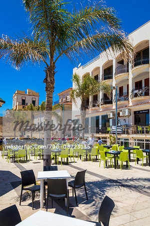 Modern tables and chairs in an open area patio surrounded by historic buildings in Marina di Ragusa in Sicily, Italy