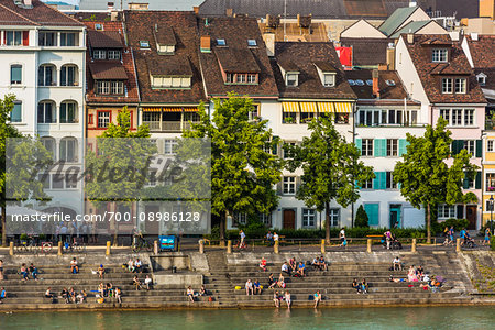 People sitting on steps along the seawall of the Rhine River in Basel, Switzerland