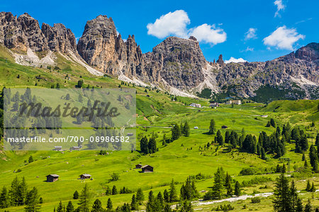 Grassy mountain side with wooden mountain huts and the jagged mountain ridge at the Gardena Pass in the Dolomites in South Tyrol, Italy