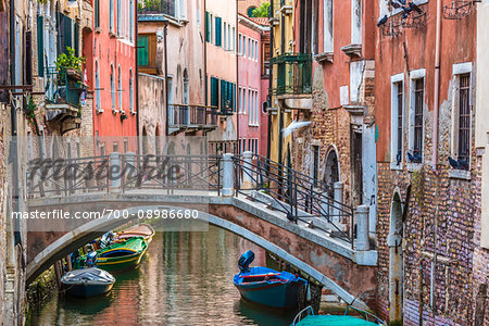 Stone footbridge with iron railing crossing a canal lined with historical buildings in Venice, Italy