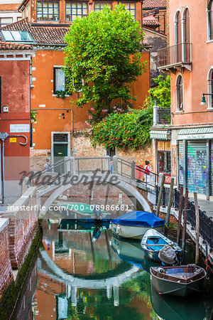 Canal with moored boats and reflection of a footbridge in Venice, Italy